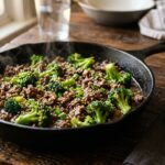 Ground beef and broccoli in a glossy brown sauce in a black skillet with sesame seeds