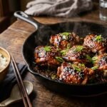 Glossy teriyaki chicken thighs in a skillet with sesame seeds and green onion